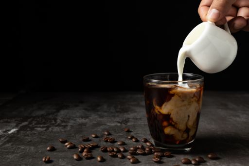 A barista pouring oat milk into a steaming cup of coffee, creating a creamy swirl.